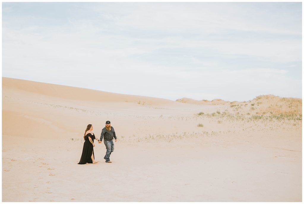 couple walking through sand dunes